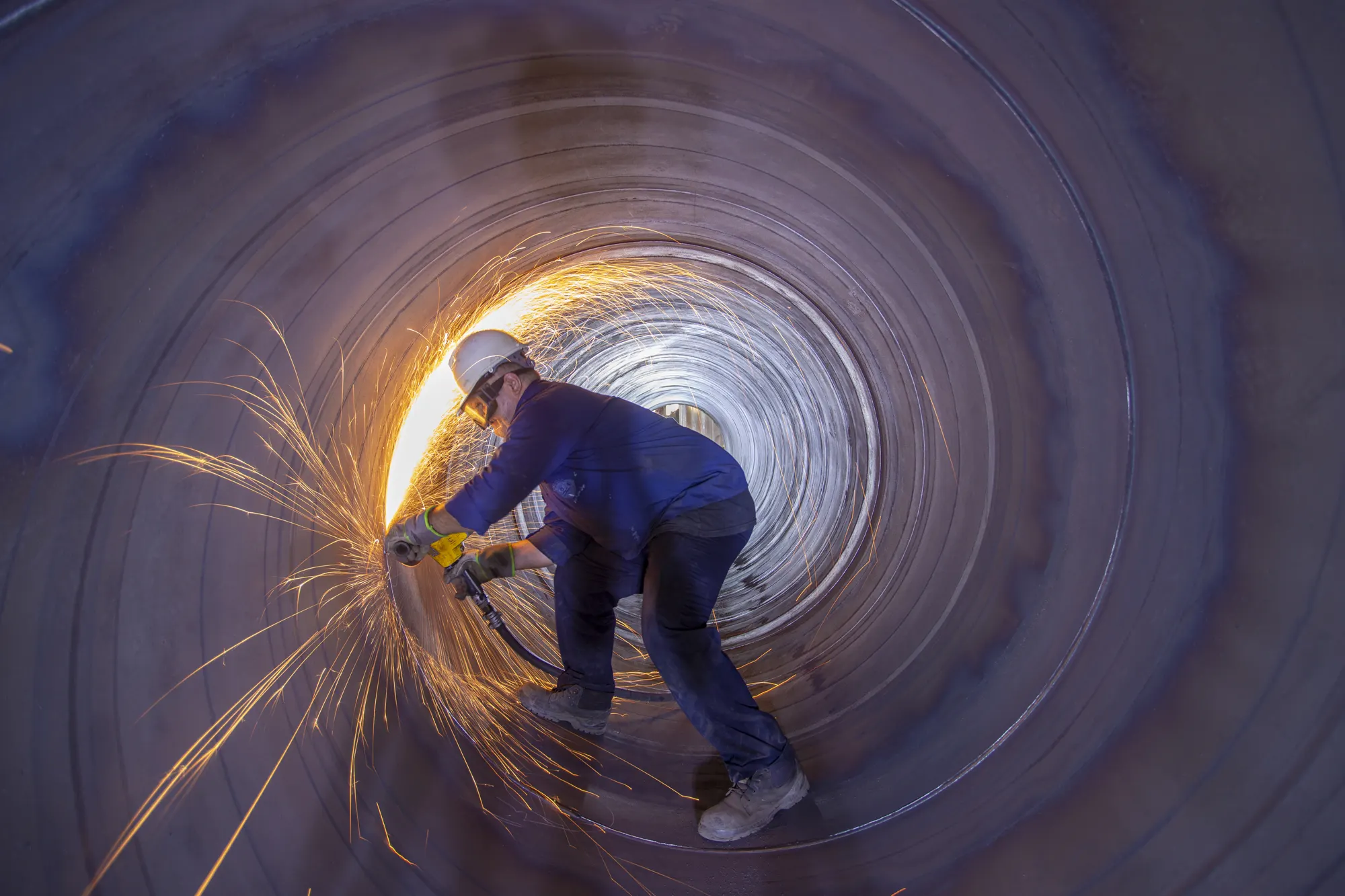 Fabricator grinding inside a large steel pipe with sparks flying